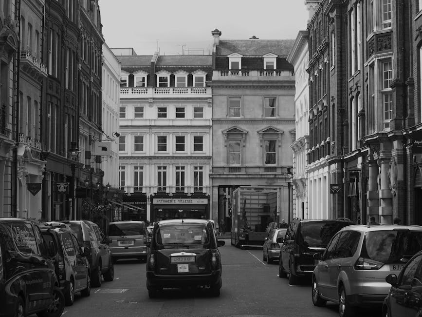 A street scene in an urban area featuring mid-rise historic buildings with varied architectural styles, including brick facades, arched windows, and a green domed tower. In the foreground, a Self Stor