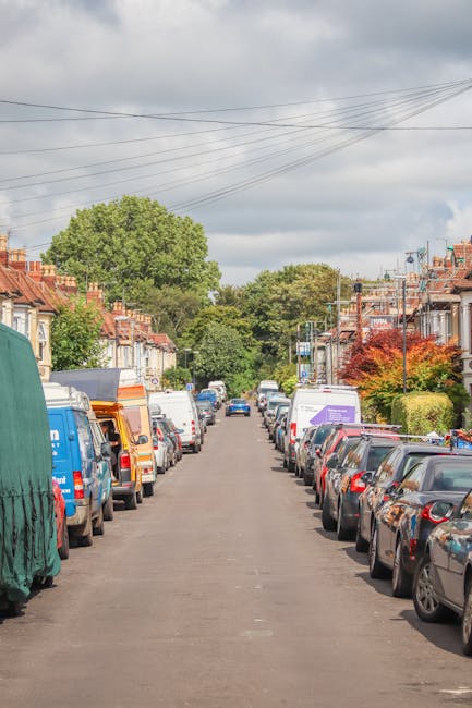 A residential street in Kentish Town with white Victorian-style terraced buildings featuring black wrought-iron balconies and decorative columns. Several parked cars, including a black van, an SUV, an